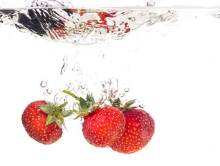 Red fresh strawberries thrown into the water, under water. Spat and splash