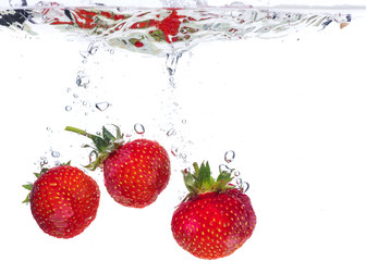 Red fresh strawberries thrown into the water, under water. Spat and splash