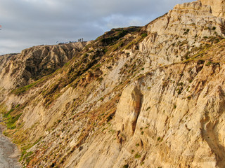 Aerial view of pacific coastline with yellow sandstone cliffs and waves rushing the beach during sunset. Black Beach, Torrey Pines State Natural Reserve, San Diego, California, USA