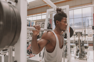 Muscular male athlete concentrating, working out with heavy barbell. African athletic man lifitng barbell at the gym. Focused strong sportsman exercicing with weights