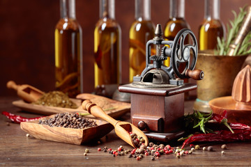 Old pepper mill with cooking utensils, bottles of olive oil, spices and rosemary on a wooden table.