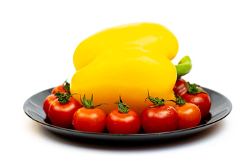 Yellow sweet pepper with tomatoes in a black plate isolated on white background. Composition of yellow peppers and red tomatoes on a white background.
