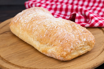 Loaf of ciabatta bread on a cutting board on the dark wooden table
