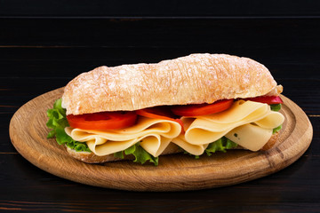 Ciabatta sandwich with lettuce , prosciutto and  cheese on wooden board