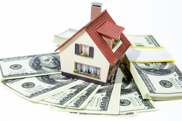 A small house lies on a fan of hundred dollar bills. The keys to the purchased house. Reduced copy of the house on a white background.