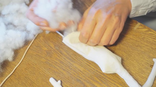 Making of handmade doll. Woman stuffing doll details with synthetic winterizer.