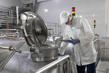Inspector in a mask and a scrub stands with a folder-tablet in his hands at the dairy plant
