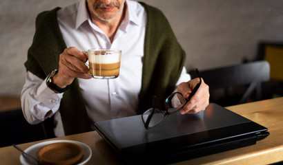 Senior man using laptop and having coffee in the bar