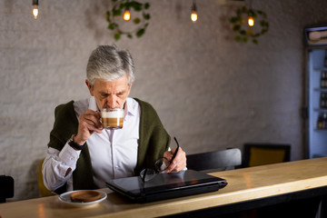 Senior man using laptop and having coffee in the bar