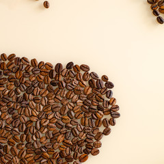 Close-up coffee beans in the lower left corner with particles on top, on a matte surface of beige color