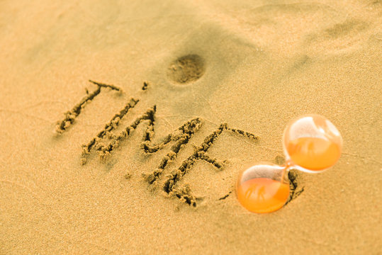 Time Equals Money Or Time Goes Fast Sign Written On The Yellow Sand Beach With Hourglass Buried In Sand. Time To Travel To Exotic Island And Have Vacation Trip To Sea Or Ocean On Holidays Take Time