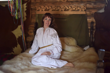 Obraz na płótnie Canvas brunette in white linen old-fashioned shirt with embroidery sits on a medieval bed with a fur skin