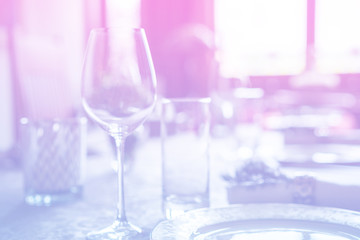 Wine glass at celebration and dining table setting with flowers decorations on light pink blue gradient background. Abstract defocused blur background. Selective focus. Toned.