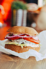 Delicious fresh homemade cheese burger with grilled meat, cheese, tomatoes, lettuce and onion rings in kraft paper. street food on wooden background
