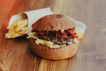 Delicious fresh homemade cheese burger with meat, cheese, tomatoes, lettuce and onion rings in Kraft paper and french fries . street food on wooden table  on wooden background