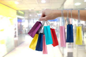 Crop female hand holding colorful paper bags on background of shopping center.