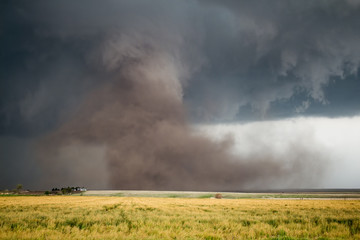 A large tornado with a huge cloud of dust fills the air under a dark supercell storm.