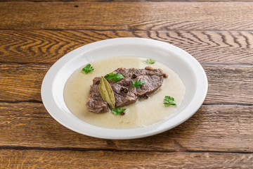 piece of boiled beef on a plate with broth isolated on wooden background