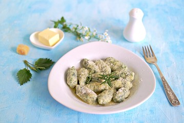 Gnocchi or dumplings with nettle or spinach on a white plate on a light blue background. Served with butter and parmesan cheese. Italian food. Selective focus