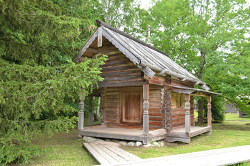 Old wooden house against the background of green grass and trees in the museum of wooden architecture.