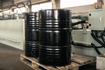 Black metal barrel of combustive-lubricating chemicals is on a wooden pallet at the production site.