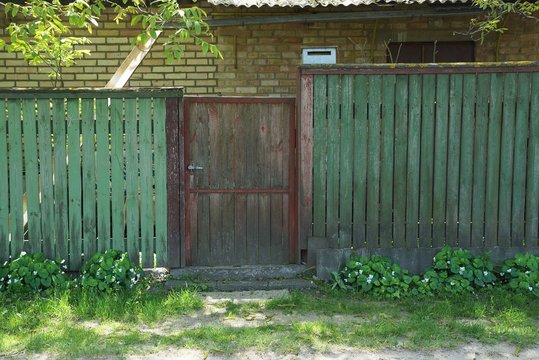 brown wooden door and green fence on a rural street in the grass
