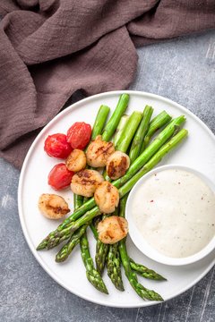 Grilled scallops and asparagus with  sauce on white plate, top view