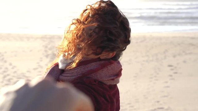 Young female saying goodbye to boyfriend and fading away into the distance. Romantic woman at the seashore beach going away from her couple on a winter day. The wind move slowly her curly hair.
