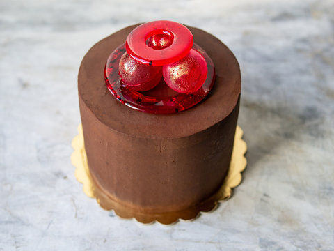 Chocolate cake covered with ganache with isomalt decor on marble gray background. Unusual decor of red isomalt - rings, balls. Copy space, selective focus, close up
