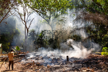 Fototapeta premium A man in a gauze bandage and a fire hose trying to put out the fire in the forest. Fire and smoke in the jungle. Fills with water. Firefighter in a rainforest