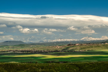 Fototapeta na wymiar A huge turbulent cloud with Cumulus clouds hung in the blue sky over the valley and villages on the background of the mountains of Gegham ridge in Armenia