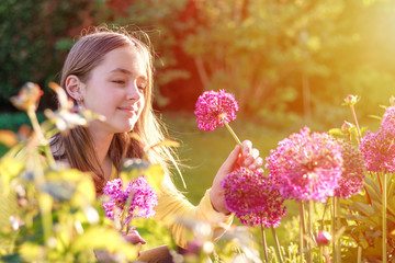 Close-up portrait of beautiful preteen girl picking up purple allium onion flowers in garden...