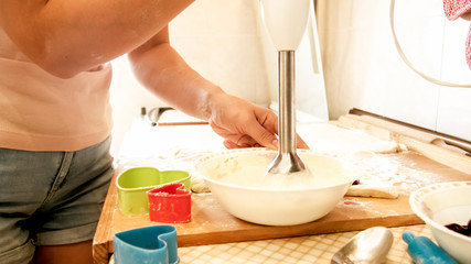 Closeup image of young woman mixing ingredients in bowl while cooking. Photo of girl using electric blender while making cream for pie or cake