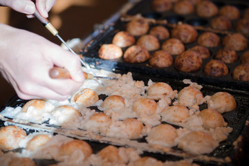 Hands of chef cooking Takoyaki ball dumplings or Octopus balls. Takoyaki balls are made with octopus, wheat flour-based batter and pan. Takoyaki is a snack and street food speciality from Osaka, Japan