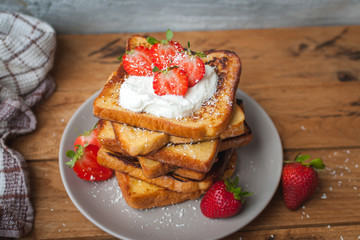 Close-up of french toast with fresh strawberries, coconut shreds and honey, on wooden background