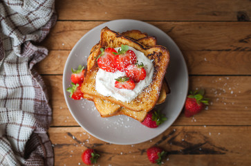 Close-up of french toast with fresh strawberries, coconut shreds and honey, on wooden background, top view