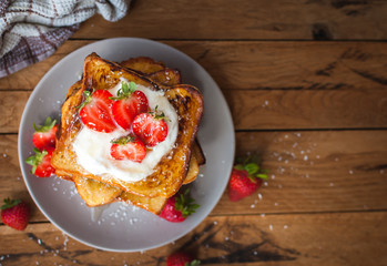 French toast with fresh strawberries, coconut shreds and honey, on wooden background, top view,...