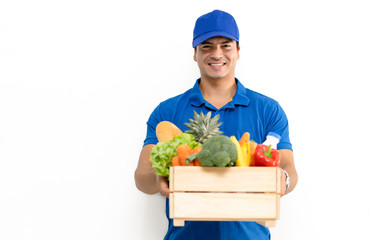 Handsome Caucasian grocery delivery courier man in blue uniform with grocery wooden box with fresh...
