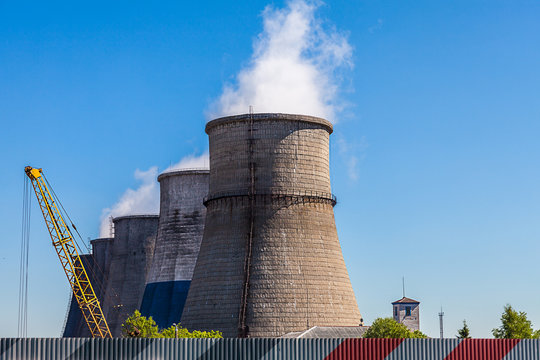Five huge brick chimney-stalks of a thermal power plant with white smoke emerging from them