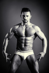 Fototapeta na wymiar Man posing in the studio on a dark background. Bodybuilder and active lifestyle. Seductive and strip theme. Attractive man with pumped biceps and stomach muscles.