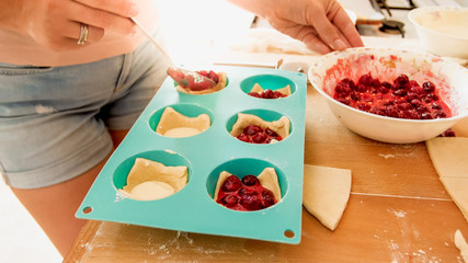 Closeup image of young woman putting fresh berry sauce in cupcakes. Woman baking cakes and pies at home