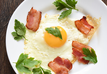 Fried eggs with slightly fried bacon and parsley on a white plate.