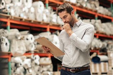 Manager reading an inventory while working on a warehouse floor