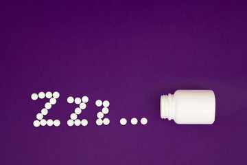 Inscription zzz made from white pills spilling from pill bottle on violet background