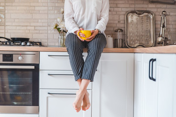 woman sitting on kitchen table with phone and yellow mug