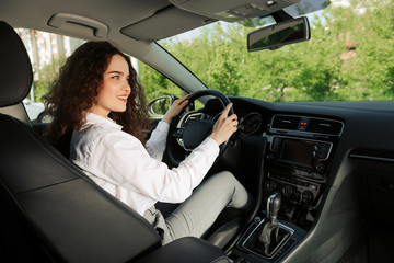 Confident and beautiful. Rear view of attractive young business woman looking over her shoulder while driving a car