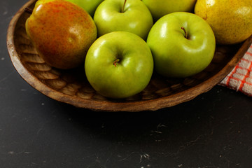 Close-up of apples and pears in wooden carved bowl on black board