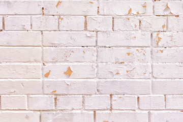 A wall of bricks of different sizes. The surface is painted light pinkish paint. Irregularities, roughness and peeling paint. Blank background for layouts.
