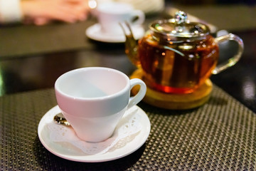 Glass teapot with blooming black tea and white cup table and dark background still life