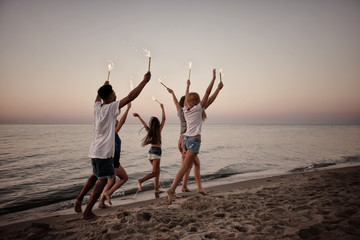 Fototapeta premium Happy smiling friends running at the beach with sparkling candles